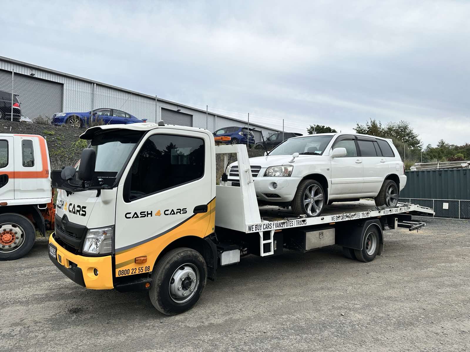 Cash 4 Cars truck with a white SUV on its flatbed in a vehicle yard